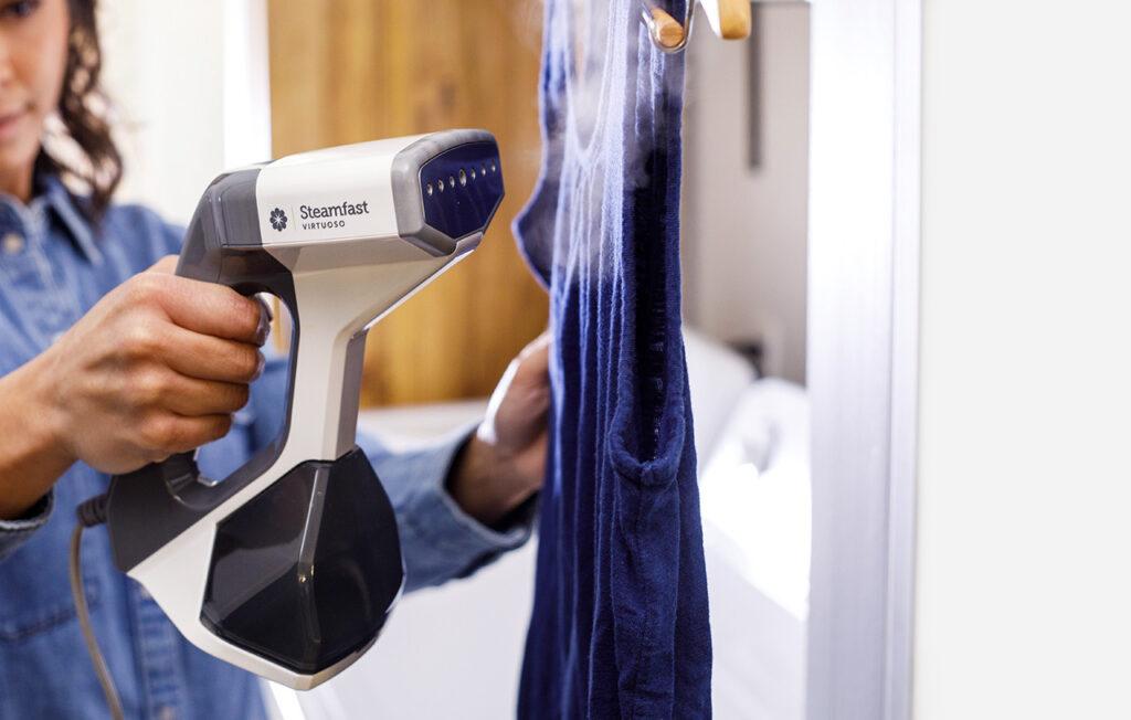Person using a handheld steamer on a blue garment in a home setting.